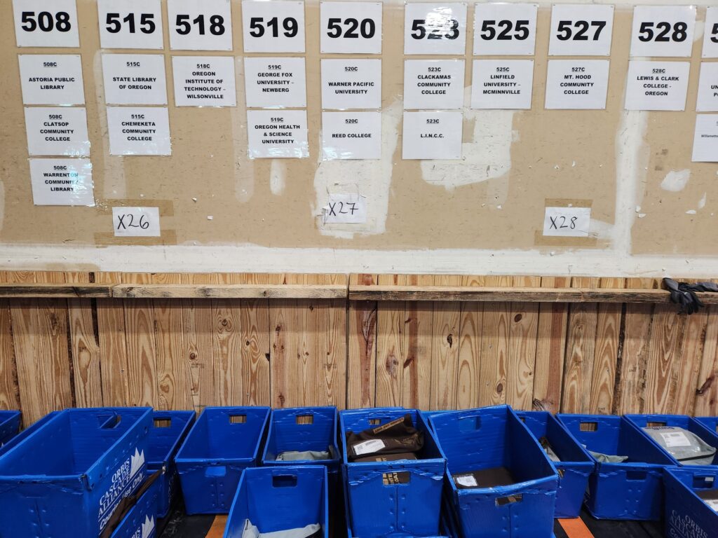 Image of the PDX Courier sorting station with each Portland destination labelled on the wall and Summit bins below.